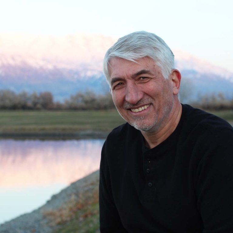 Samuel Smith posing at a lake-side with a mountain in the background.